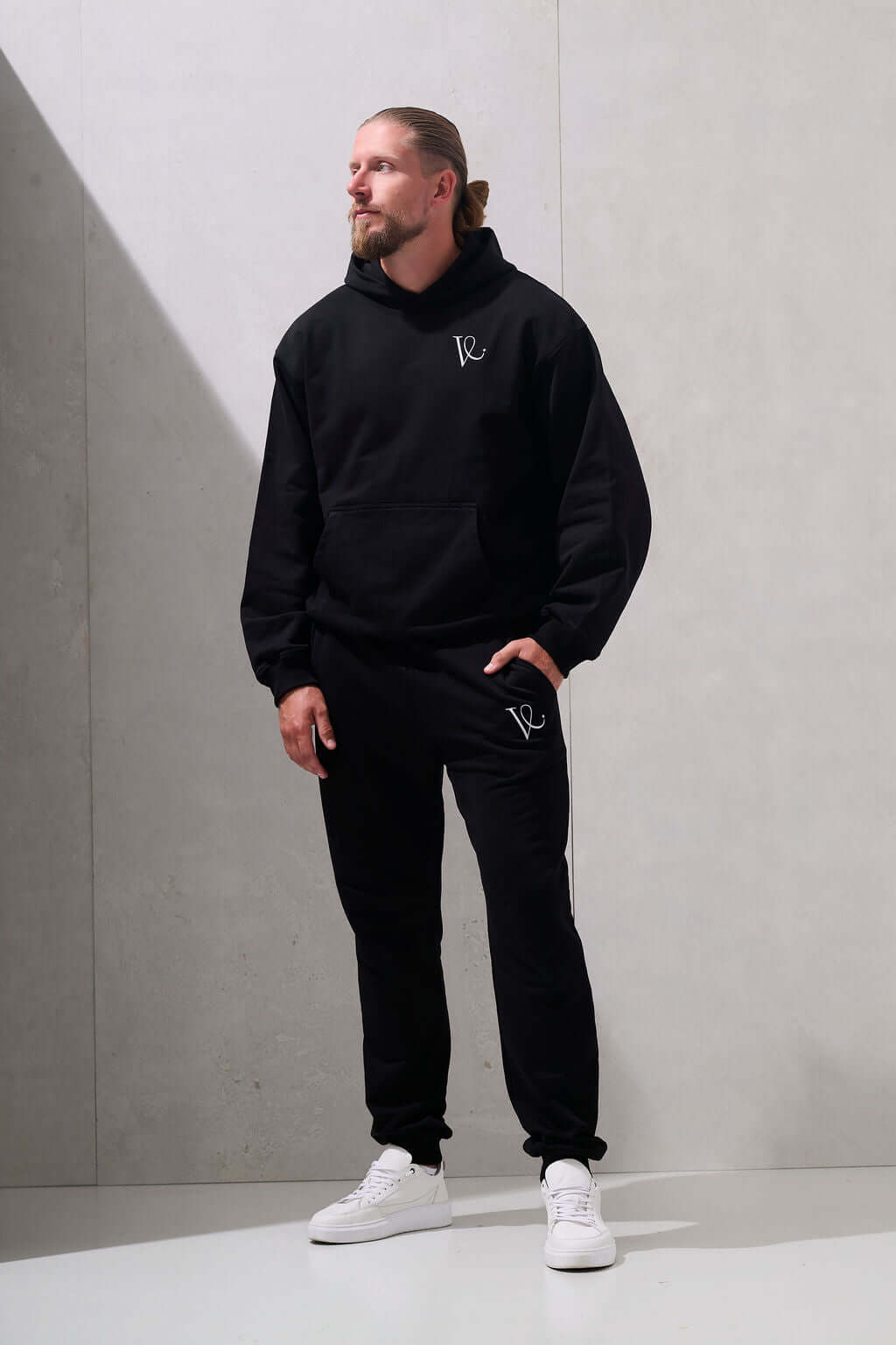 Man wearing black oversized hoodie with matching black joggers, full body front view - KAVEON